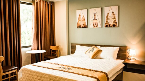 Een hotelkamer met een groot bed, een kleine tafel en een stoel. Boven het bed hangen drie afbeeldingen in lijsten.