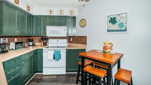 Uma cozinha compacta com armários verdes, fogão branco, micro-ondas e uma pequena mesa de jantar com banquetas.