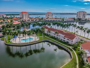 A resort with a central pool, palm trees, and buildings with red roofs.