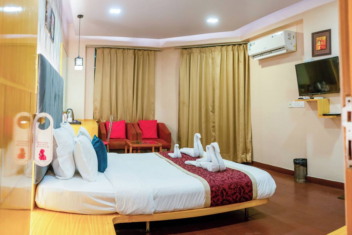 Een hotelkamer met een bed, een rode bank, een televisie en een airconditioning.