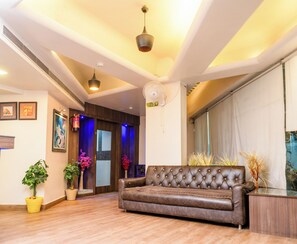 Ampla sala de estar com sofá de couro, piso de madeira e ventilador de teto.