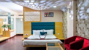 Een hotelkamer met een bed, een rode fauteuil, een klein tafeltje en een decoratief wandpaneel.