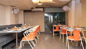 Een restaurant met een lange toonbank, oranje stoelen en een bank. Er staan tafels en stoelen klaar voor gasten.