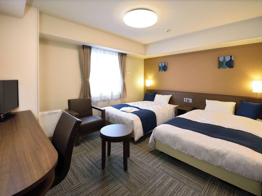 Een hotelkamer met twee bedden, een bureau, een stoel, een televisie en een klein tafeltje.
