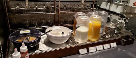 A breakfast bar with various beverages, including apple juice and orange juice, and a bowl of cereal.