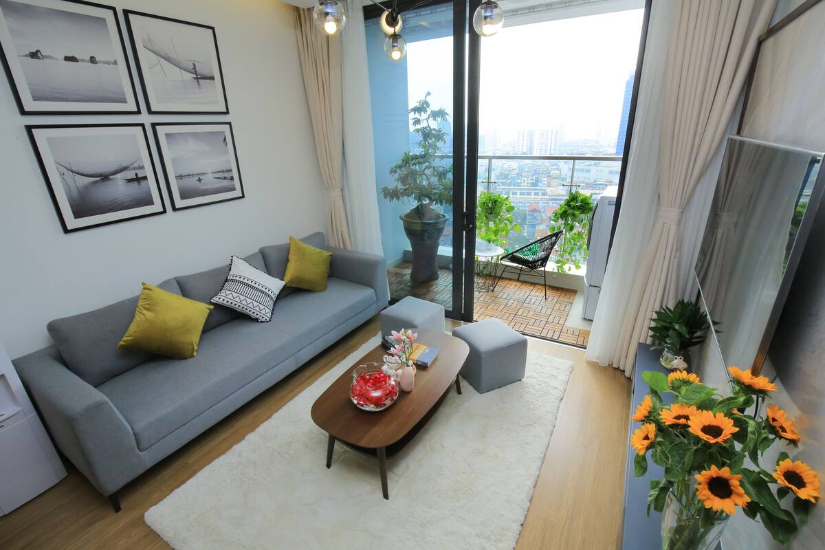 Un salon moderne avec un canapé gris, une table basse et une vue sur le paysage urbain à travers de grandes fenêtres.