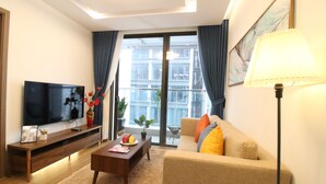 Een moderne woonkamer met een flatscreen televisie, een houten tv-meubel, een bank, een salontafel en een groot raam met gordijnen.