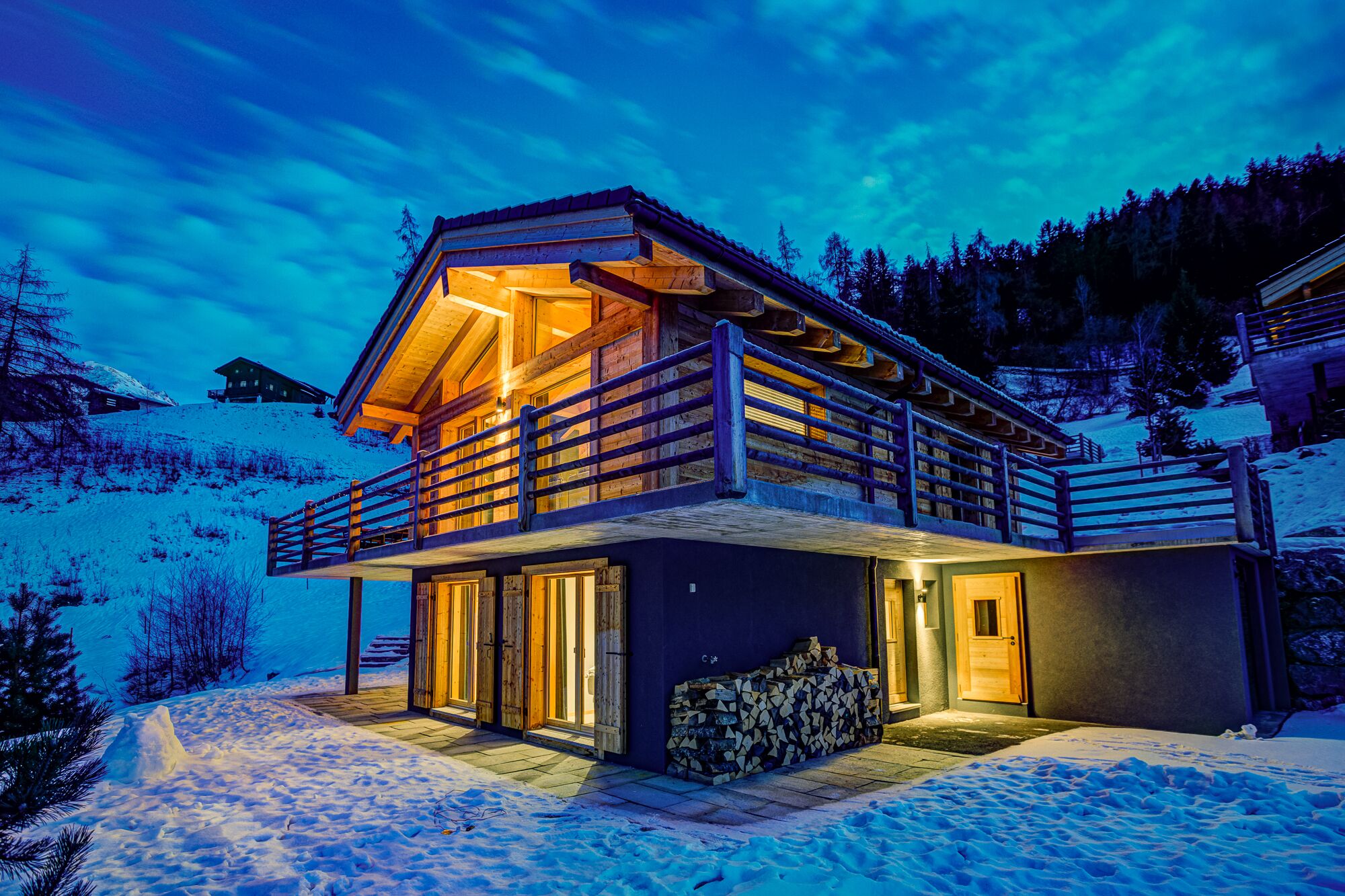 Eine Holzhütte mit Balkon, verschneiter Erde und einem Bergpanorama im Hintergrund.