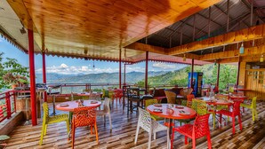Un espace de restauration en plein air doté d’un plancher en bois et de chaises colorées, offrant une vue sur un paysage montagneux.