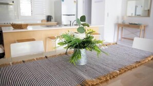 A dining area with a table set for two, a potted plant, and a kitchen in the background. - Unit 88 - Tropical Getaway in 2 Bedroom Unit in 4* Resort (Noosaville)