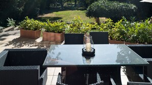 An outdoor patio with a glass table and wicker chairs, surrounded by greenery and trees. - Hotel Villa im Park (Düsseldorf)