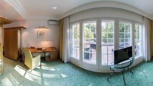 A spacious room with a large bay window, a television on a glass table, a sofa, and a chair. - Hotel Villa im Park (Düsseldorf)