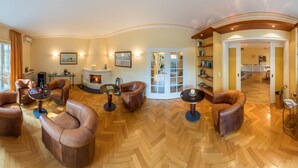 A spacious lounge area with leather armchairs, a fireplace, and a view of the outdoor patio. - Hotel Villa im Park (Düsseldorf)