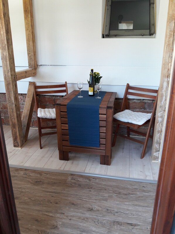 A wooden table with a blue cloth, two chairs, a bottle of wine, and a vase with flowers. - Apartment Dandelion (Wolfshagen im Harz)