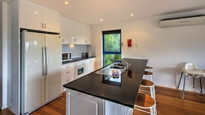 A modern kitchen with white cabinets, a black countertop, a stainless steel sink, and a window with a view of greenery.
