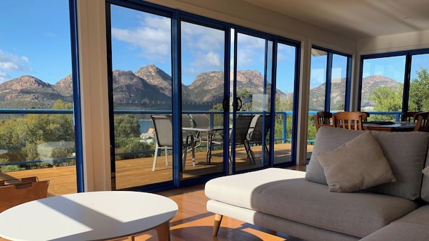 A modern living room with a large sofa, a small table, and a view of mountains through large windows.