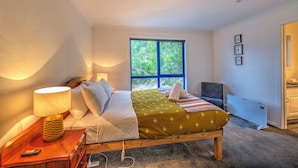 A bedroom with a bed, bedside lamps, a window with a view of trees, a chair, and a radiator.