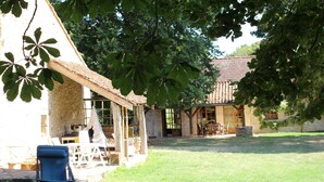 Un bâtiment rustique en pierre, doté d’un patio couvert, d’une chaise bleue et d’une pelouse.