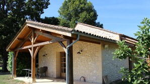 Un bâtiment en pierre avec un toit en tuiles, un patio couvert avec des chaises et une porte.