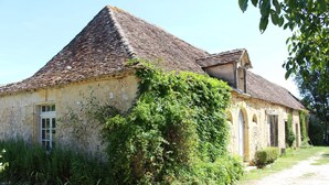 Un bâtiment rustique en pierre, doté d’un toit à forte pente, partiellement recouvert de lierre, et un chemin de terre qui y mène.
