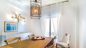 A dining area with a wooden table, chairs, a chandelier, a framed picture, and sheer curtains.