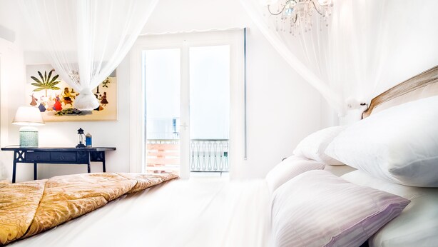 A bedroom with a bed, a desk, and a balcony.