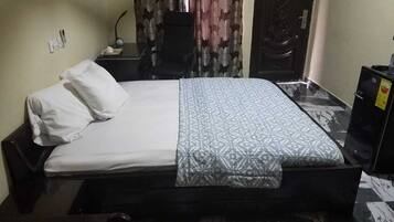 A single bed with a patterned bedspread, a bedside table with a lamp, and a curtain with a floral design.