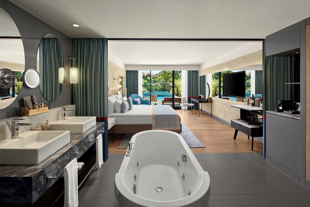 Habitación de hotel moderna con una bañera grande, una cama doble, un televisor y vistas al exterior.