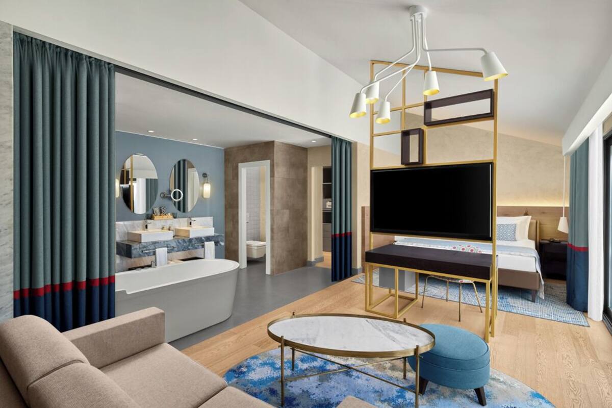 A modern hotel room with a living area, a separate bathroom, a bed, and a TV.