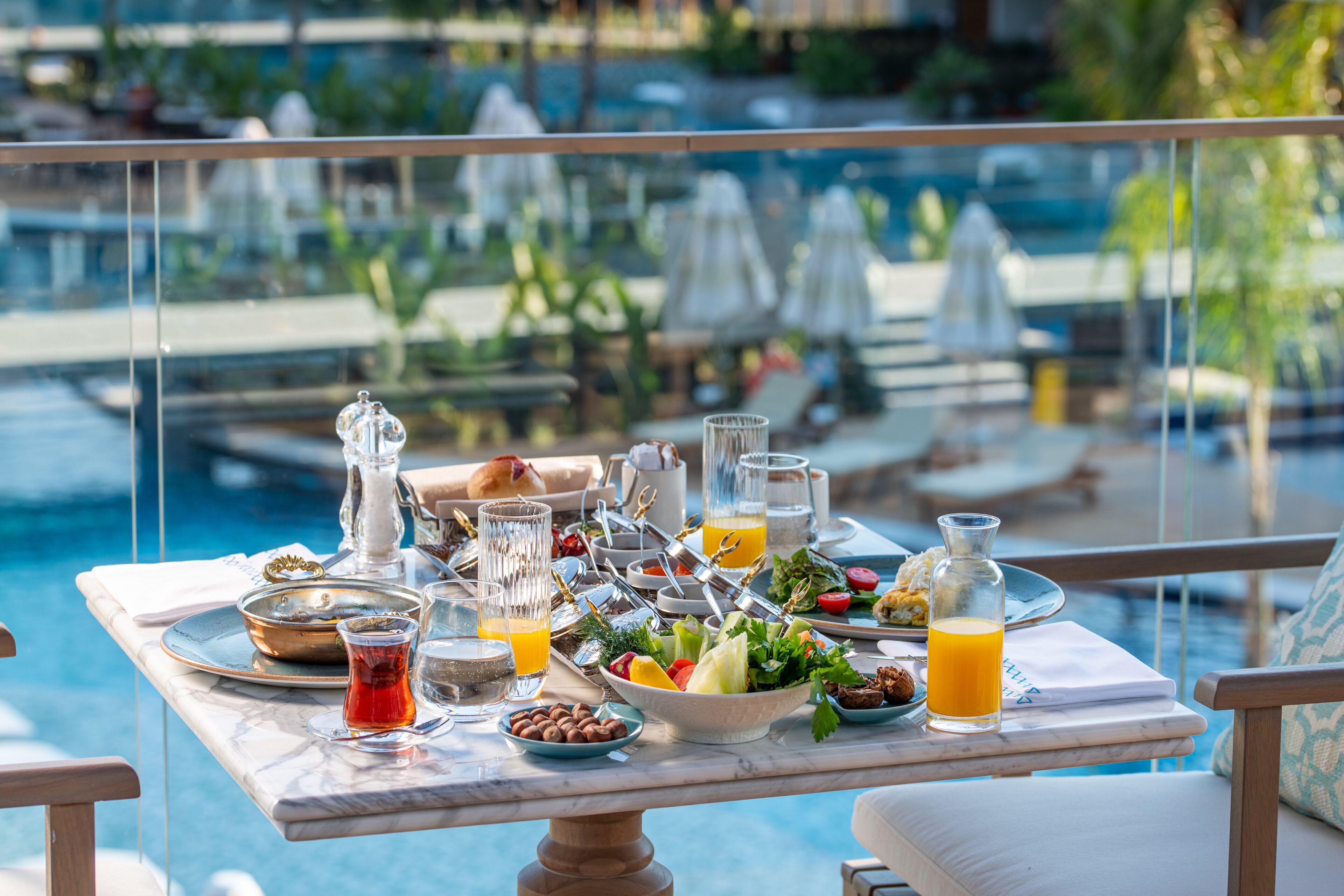 A breakfast table with a variety of food and drinks, overlooking a pool area.