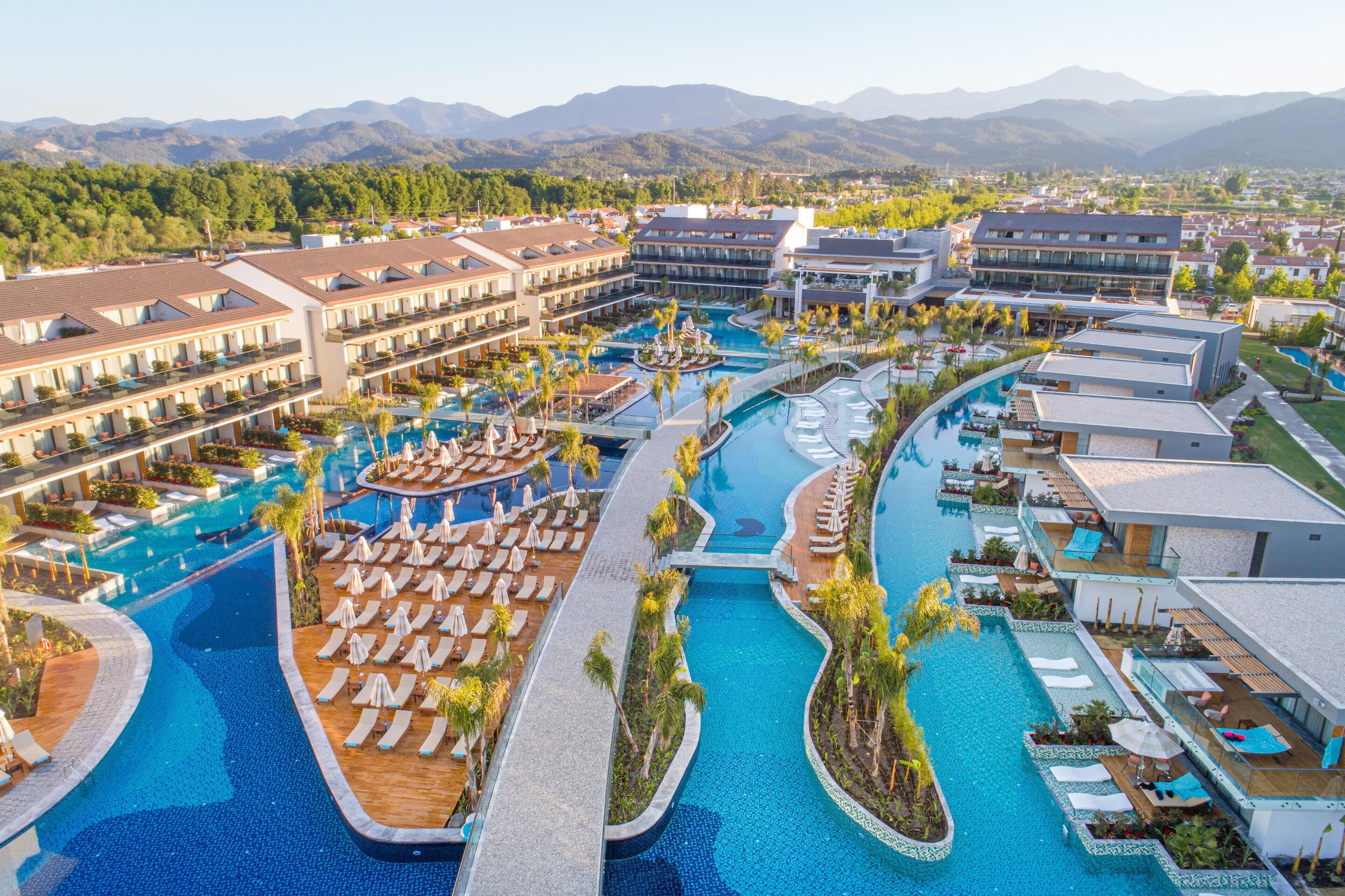 A resort with multiple swimming pools, sun loungers, and a mountainous backdrop.