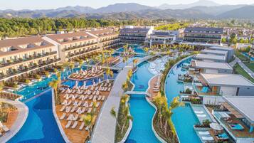 A resort with multiple swimming pools, sun loungers, and a mountainous backdrop.