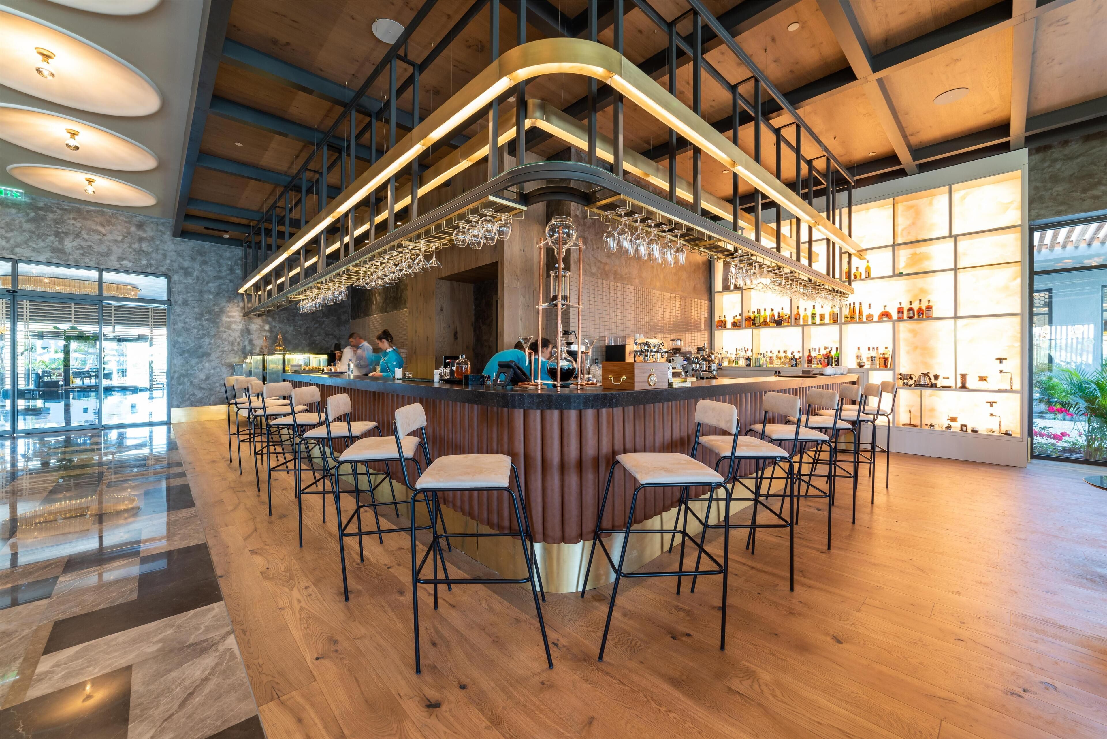 A modern bar area with a curved counter, multiple bar stools, and a variety of bottles and glasses.