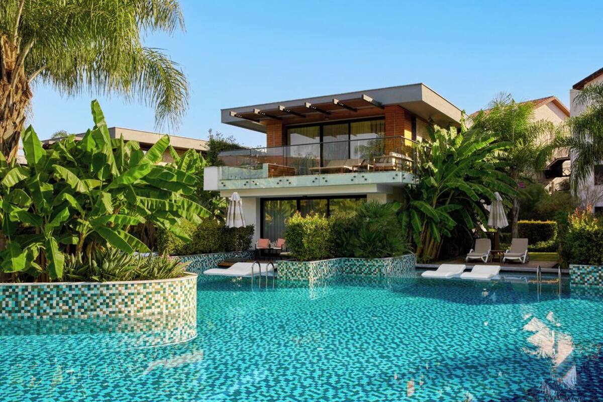 A modern pool area with a glass balustrade, lounge chairs, and a two-story building with a balcony.