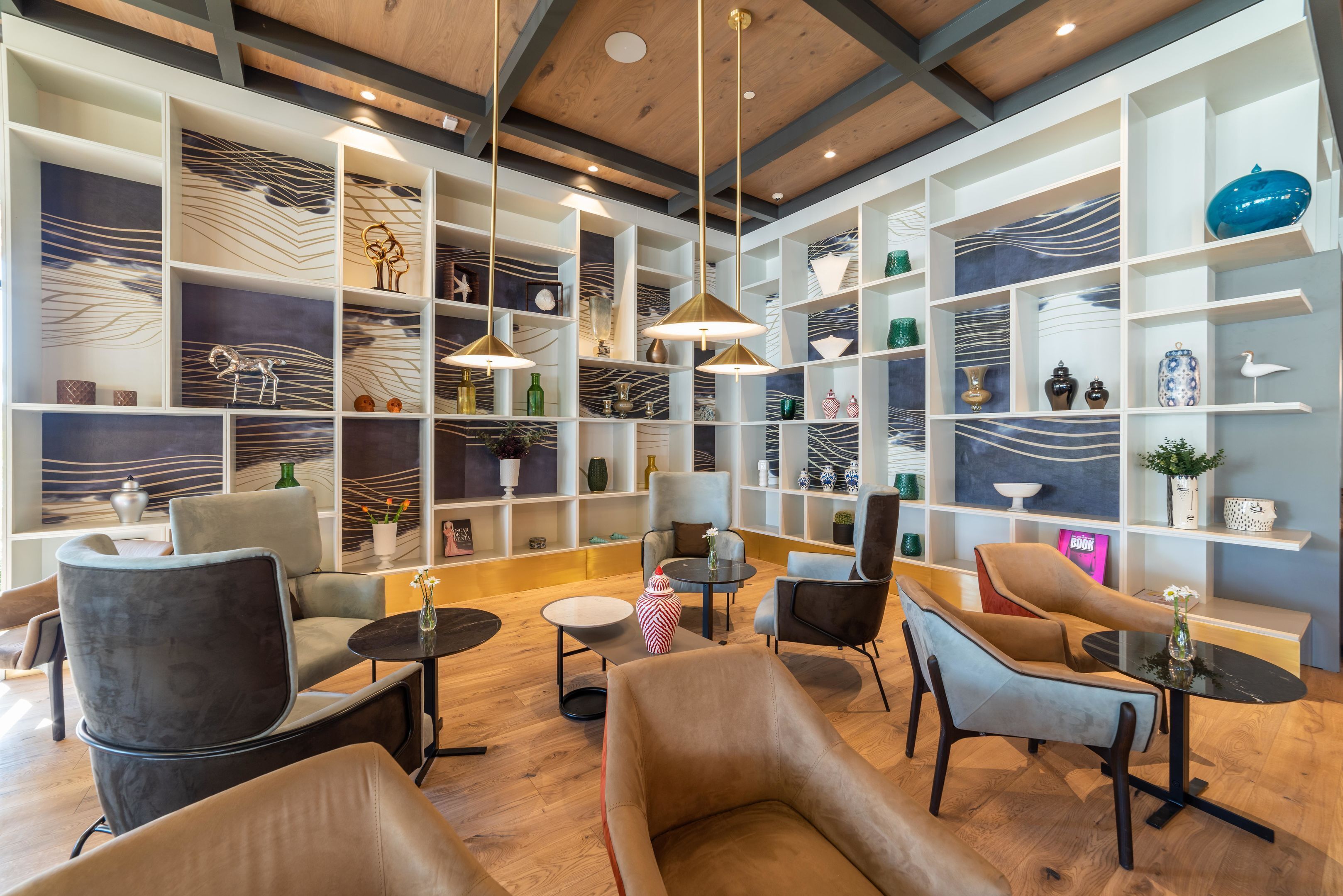 Un interior moderno con techo de madera, estanterías blancas con objetos decorativos y muebles contemporáneos.