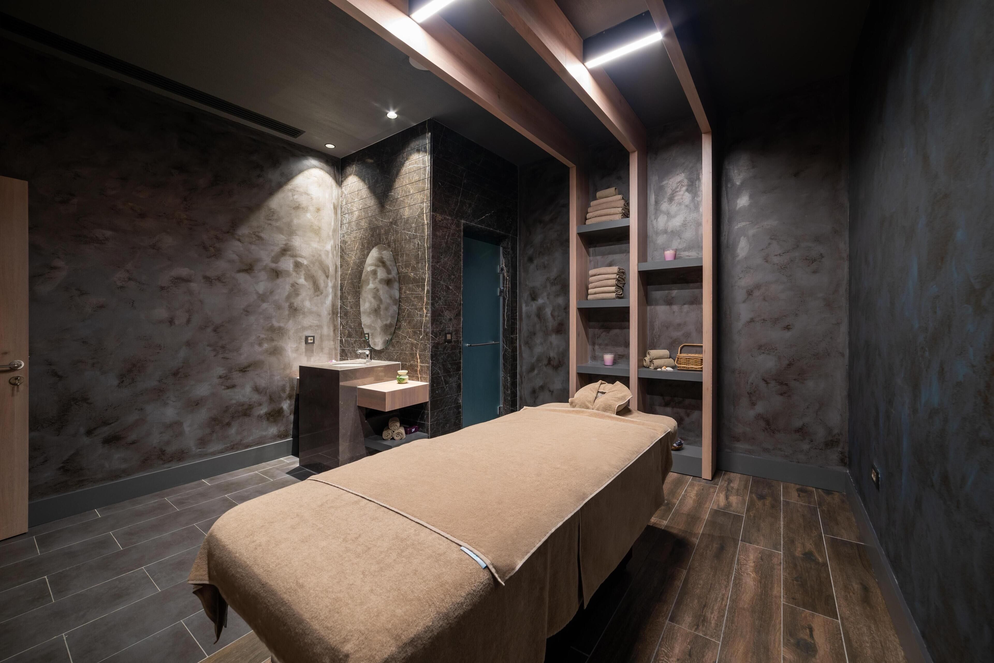 Una moderna sala spa con un lettino da massaggio, un lavandino e scaffali con asciugamani e prodotti per la cura personale.