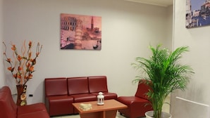 A modern living room with a red sofa set, a wooden coffee table, a potted plant, and a cityscape painting on the wall. - Hotel Nettuno (Montecatini Terme)