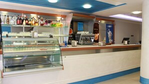 A bar area with shelves of liquor bottles, a coffee machine, and a glass display case. - Hotel Nettuno (Montecatini Terme)