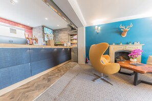 Zona de recepción con escritorio, pared azul decorada con cabeza de ciervo, chimenea y alfombra estampada.
