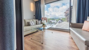 A modern living room with a sofa, a glass coffee table, and a view of a village through large windows. - The Fisherbeck (Ambleside)
