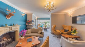 A modern living room with a fireplace, a chandelier, and a view of the outdoors. - The Fisherbeck (Ambleside)