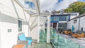 A covered outdoor seating area with wicker furniture and a glass balustrade. - The Fisherbeck (Ambleside)