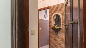 A hallway with a wooden door, a clock, and a wall-mounted flower arrangement. - Cozy Flat Borgo Pio (Rome)