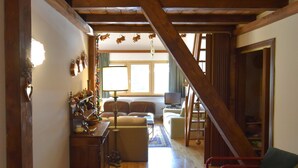 A spacious living room with a high ceiling, wooden beams, a television, and a staircase leading to another level. - EMERALD CENTRALE 022143-AT-615468 (Madonna di Campiglio)