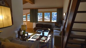 A living room with a sofa, two armchairs, a coffee table, and a lamp. There is a window with curtains, a radiator, and a staircase. - EMERALD CENTRALE 022143-AT-615468 (Madonna di Campiglio)