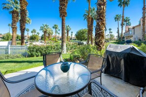 A patio with a round glass table, metal chairs, and a grill. - Beautiful 2BR Townhome in PGA West (La Quinta)