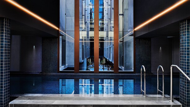 Zona de piscina interior moderna con vistas a un edificio alto a través de paneles de vidrio.