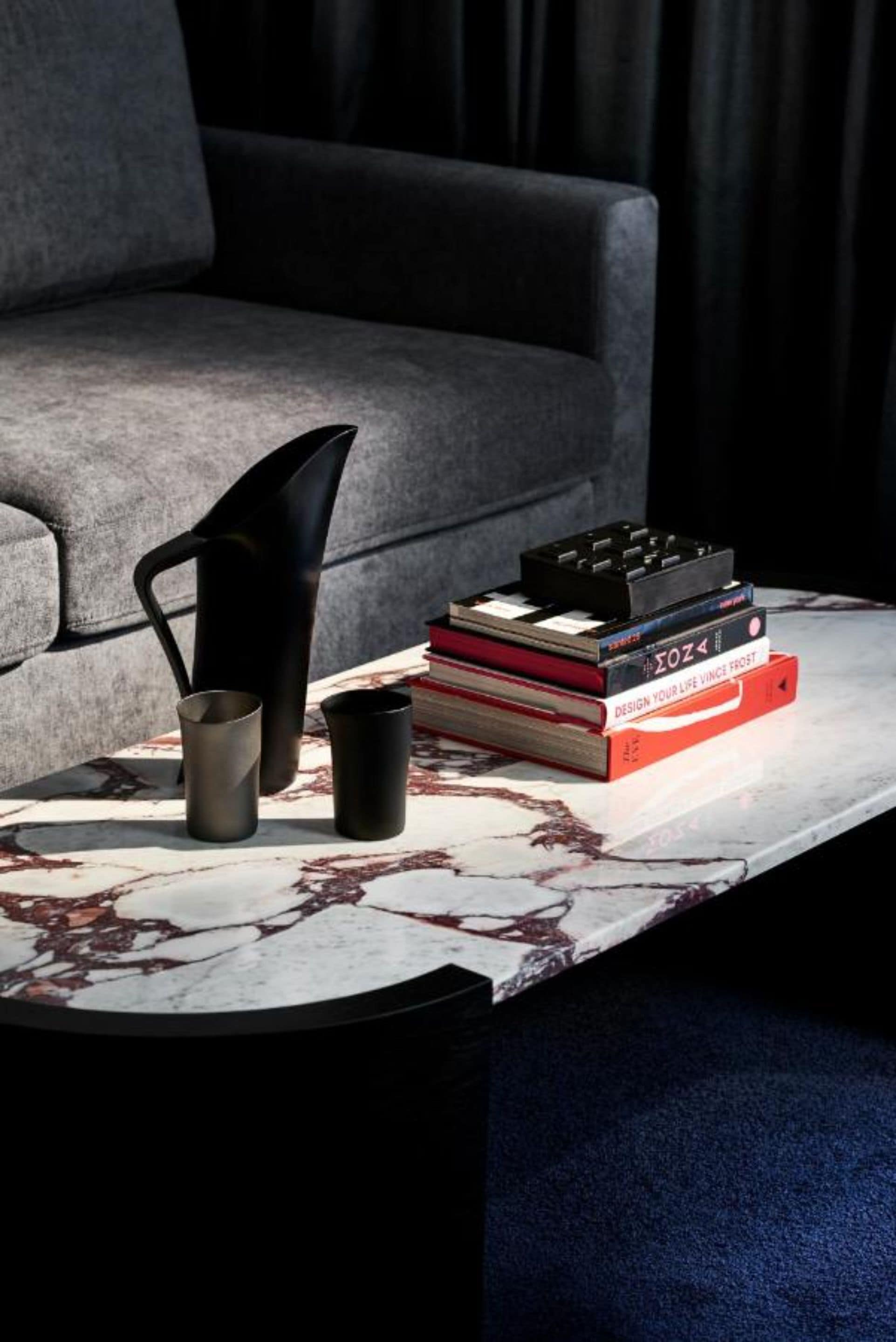 A modern living room with a grey sofa, a marble coffee table, and a stack of books.