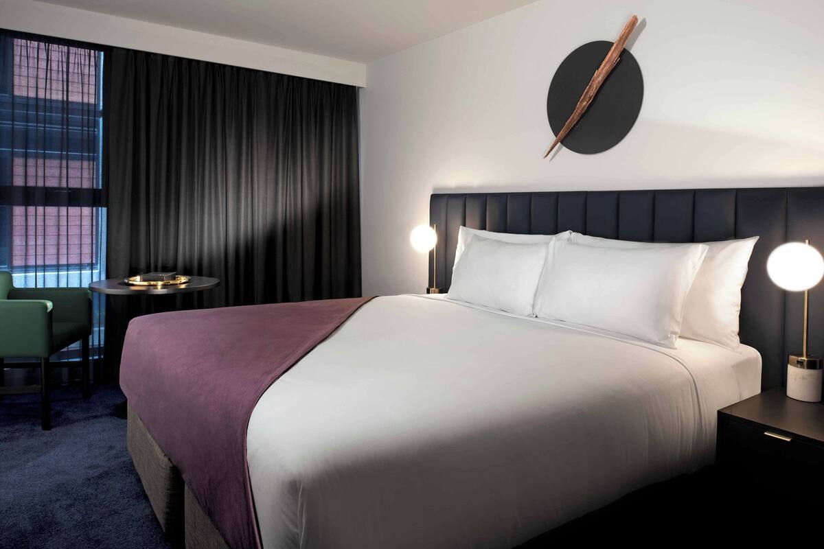 A hotel room with a large bed, a desk, a chair, and a window with curtains.