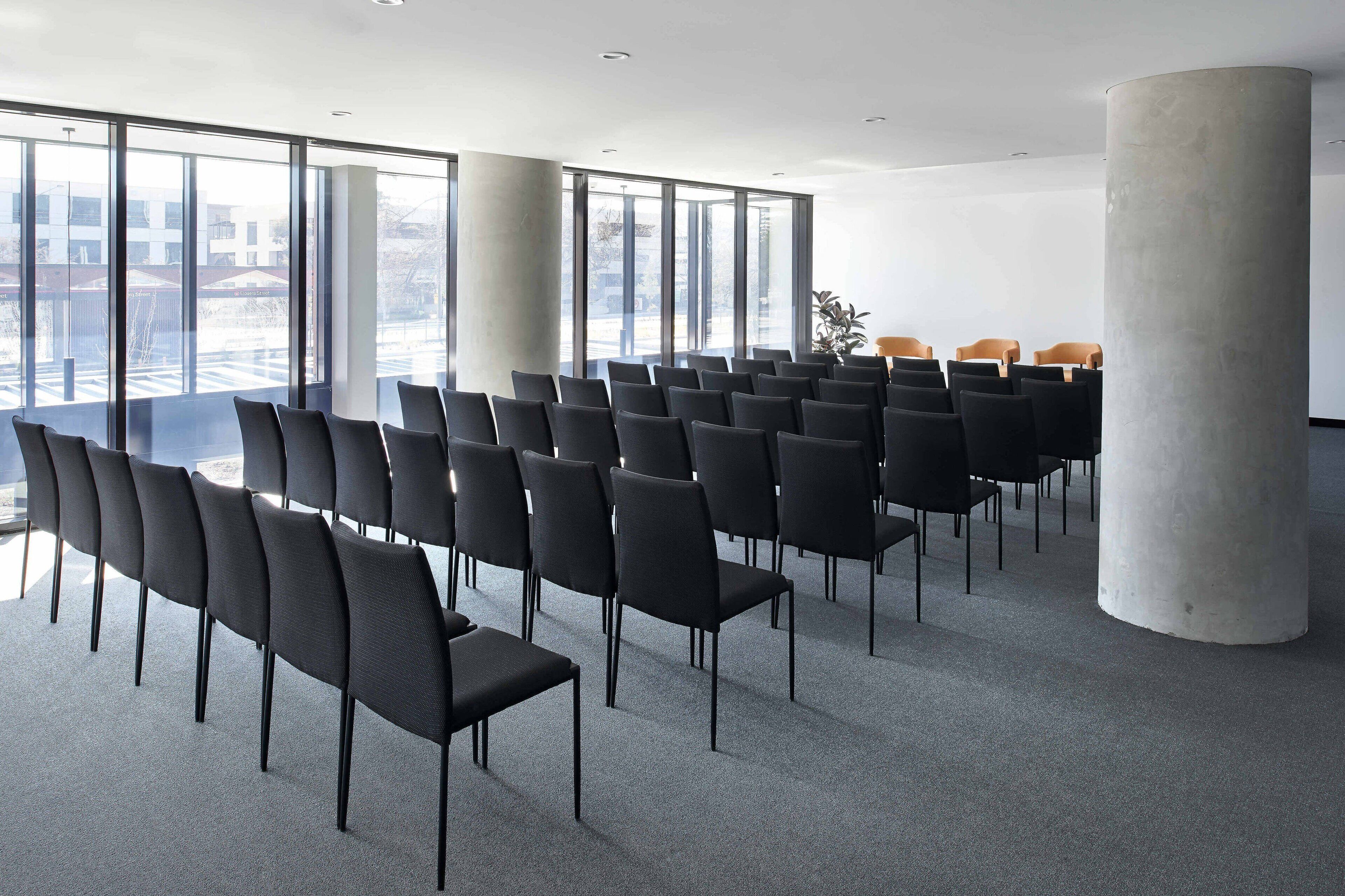 A conference room with rows of chairs, large windows, and a concrete pillar.